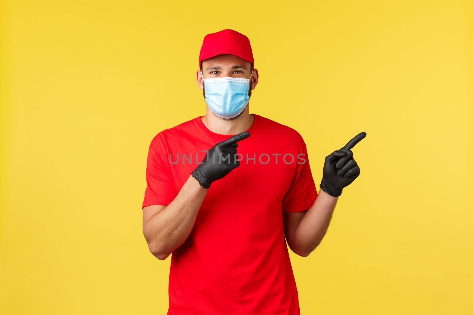 Express delivery during pandemic, covid-19, safe shipping, shopping concept. Friendly courier in red uniform, medical mask and gloves, inform clients about safe contactless deliver, point right.