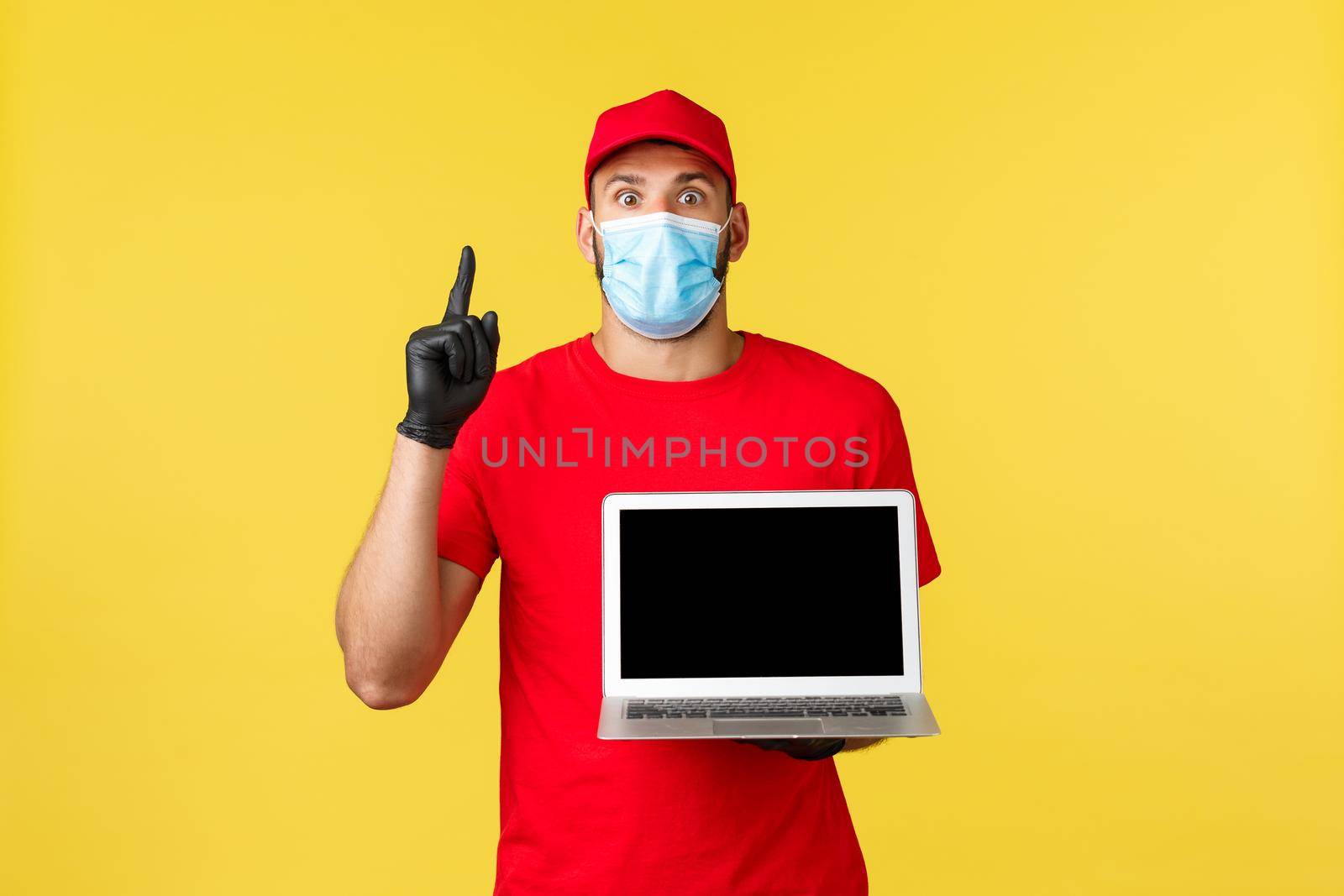 covid-19, safe shopping, express delivery, order tracking concept. Creative and thoughtful courier in red uniform and medical mask, raise index finger as showing awesome link, banner on laptop screen.