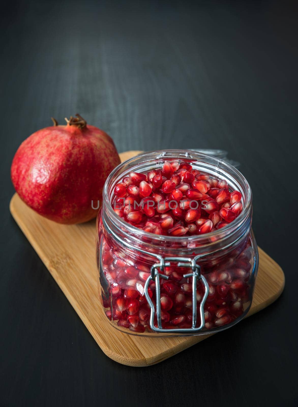 Delicious pomegranate seeds placed in glass jar with fresh organic pomegranates on rustic wooden background.Close up,Copy space by DaLiu