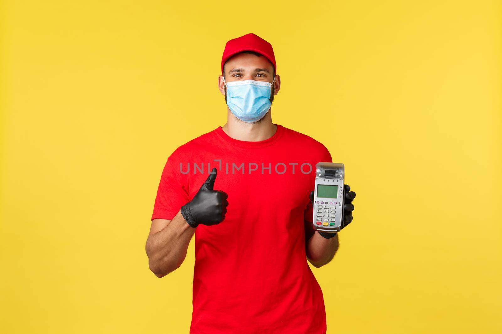 Food delivery, tracking orders, covid-19 and self-quarantine concept. Courier encourage clients use contactless payment option on site while ordering in internet, showing POS terminal and thumb-up.