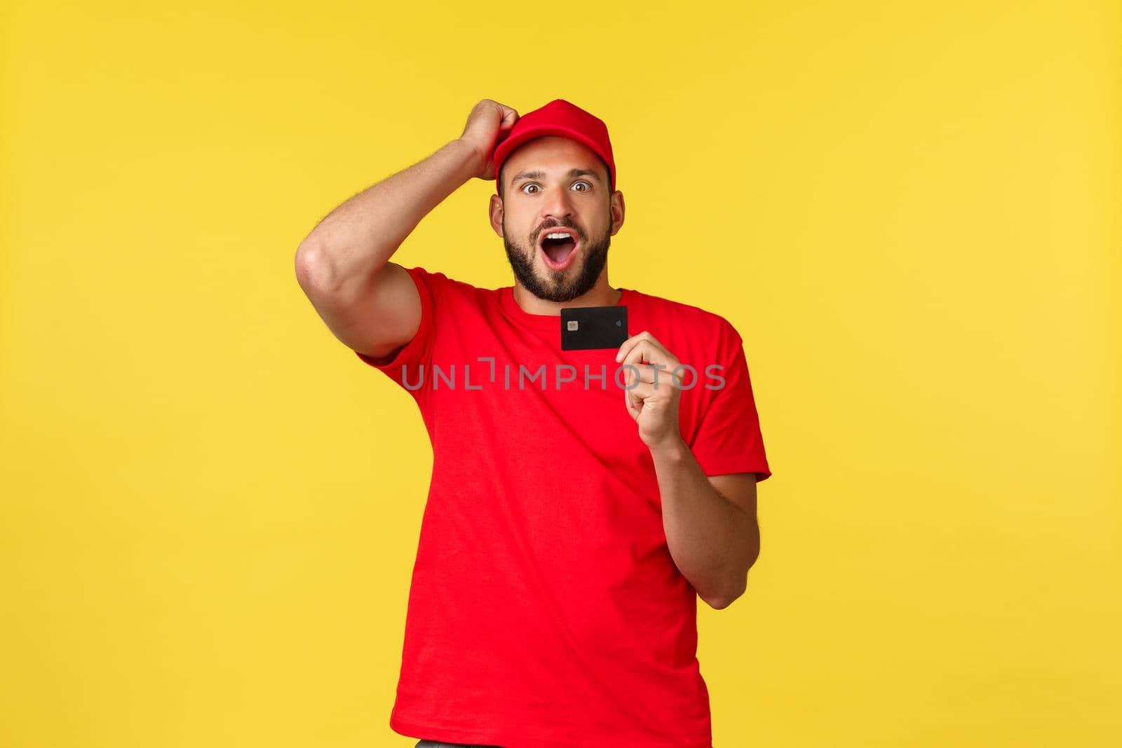Contactless payment, online delivery, internet shopping concept. Excited and astonished courier, male employee in red uniform cap and t-shirt, showing credit card, impressed with new features.