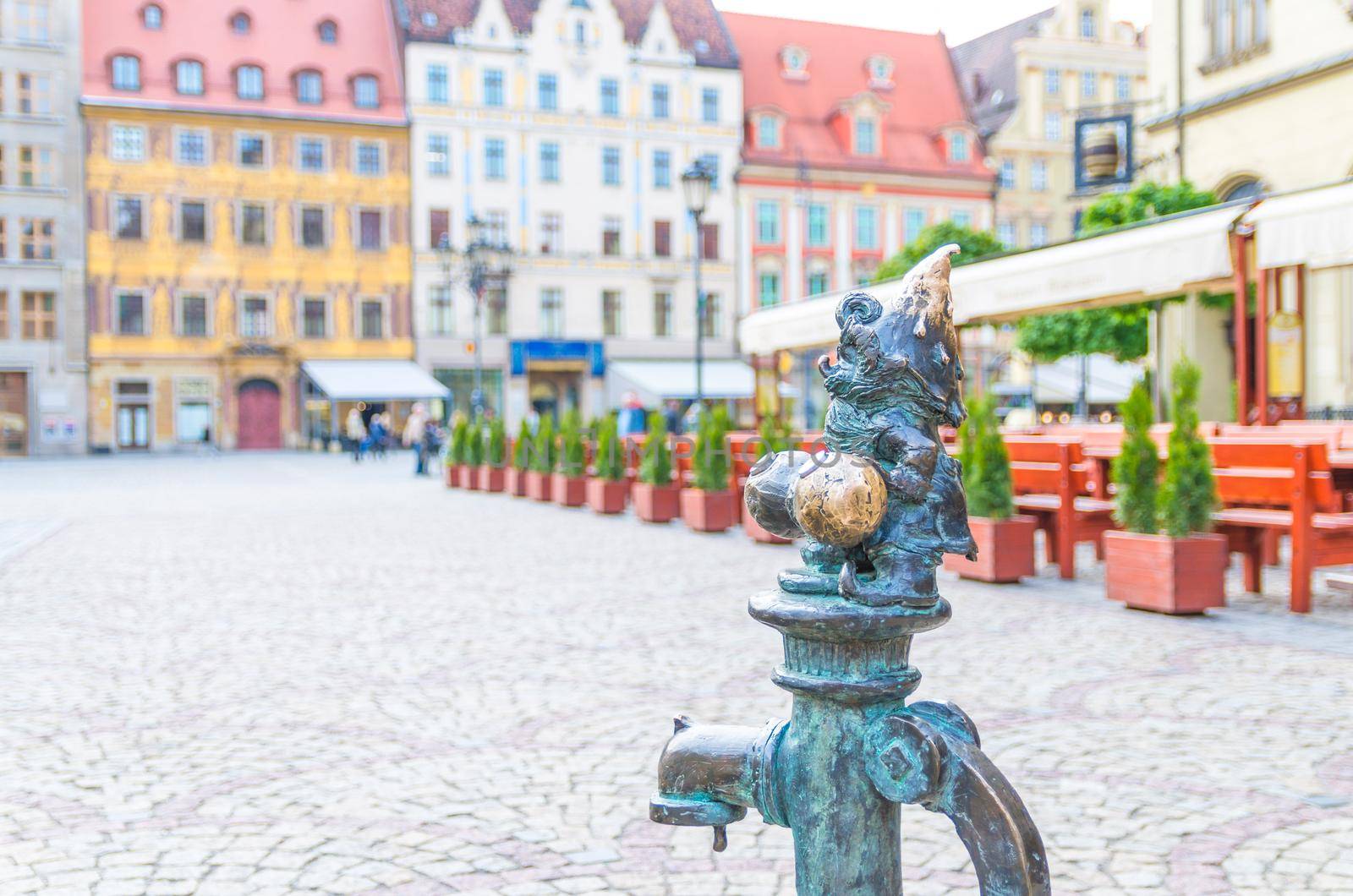Wroclaw, Poland, May 7, 2019: Dwarf is sitting on street water tap on Rynek Market Square, famous bronze miniature gnome with hat sculpture is a symbol of Wroclaw in old historical city centre