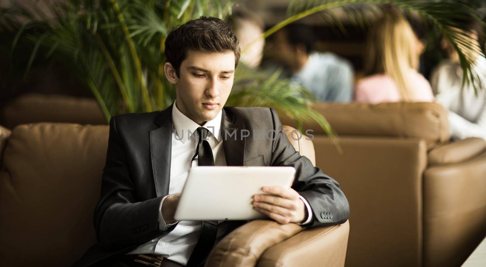 Entrepreneur-beginner with a digital tablet sitting on the couch in the background of a modern office