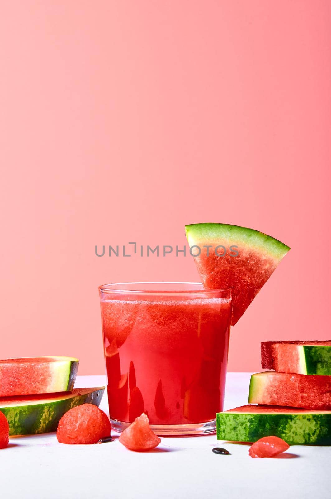 Fresh watermelon juice or smoothie in glasses with watermelon pieces on pink background. Refreshing summer drink.