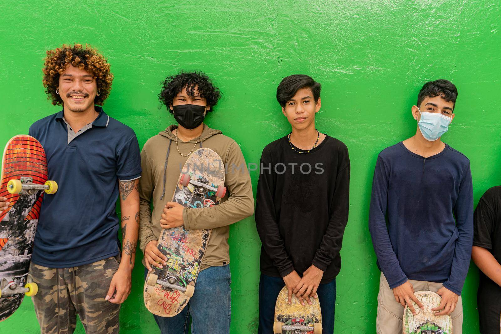 Latino teenagers leaning against a wall and looking at the camera smiling with their skate boards in their hands by cfalvarez