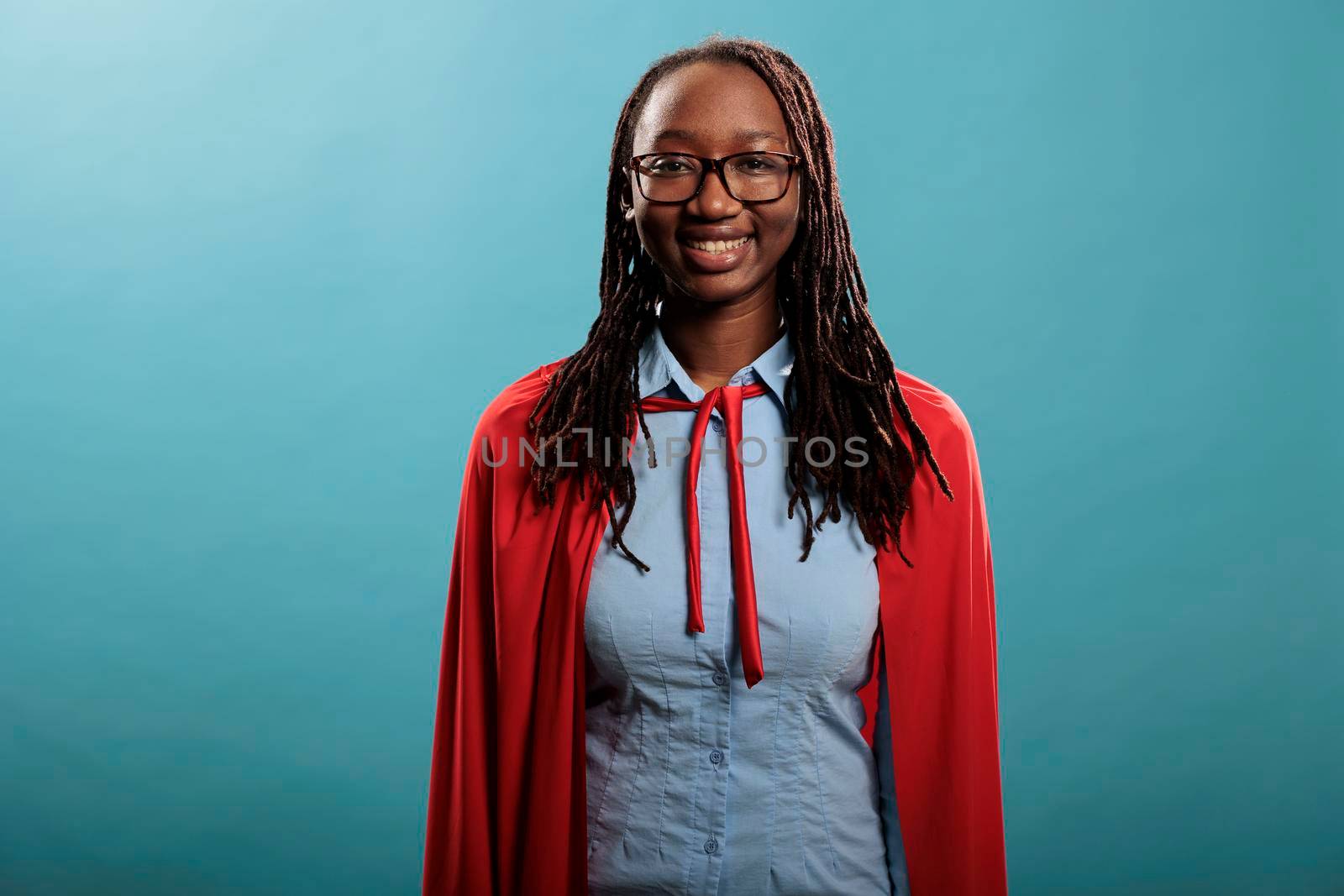 Optimistic looking superhero woman wearing hero costume while smiling heartily at camera on blue background. by DCStudio