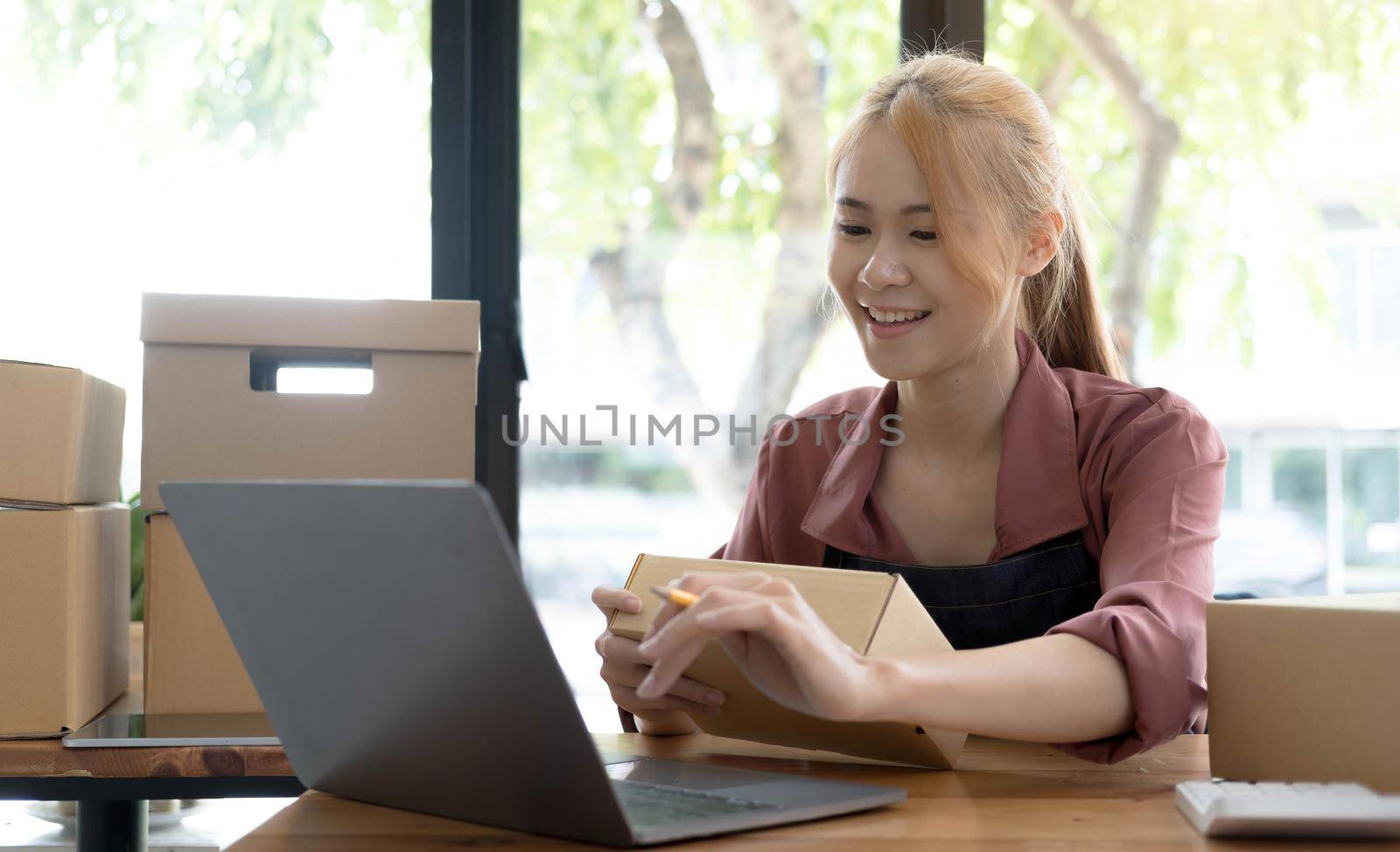 Portrait of Asian young woman SME working with a box at home the workplace.start-up small business owner, small business entrepreneur SME or freelance business online and delivery concept. by wichayada