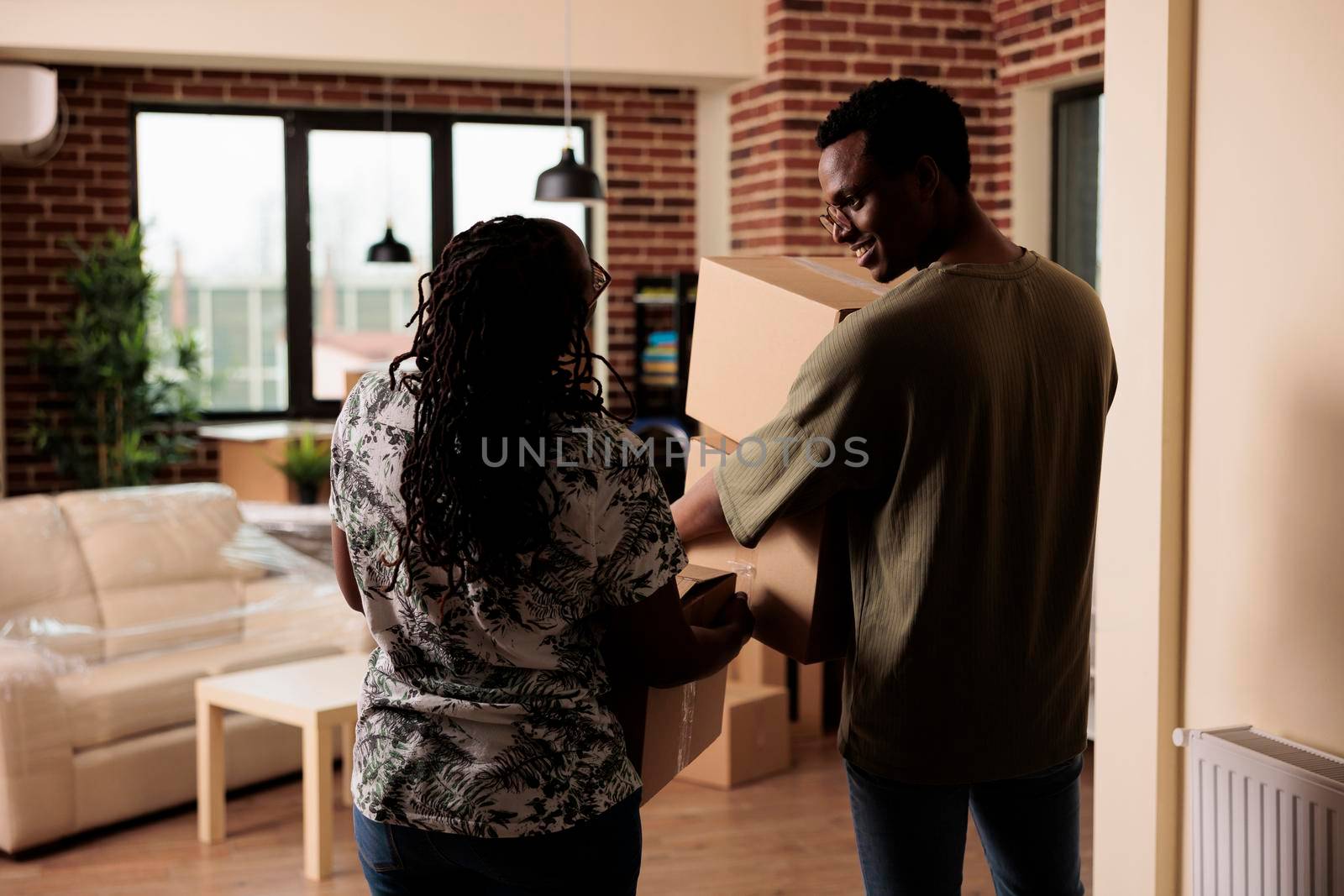 African american people carrying furniture to move in new apartment property, using boxes to decorate rented household. Moving in house together to start new beginnings on loan.