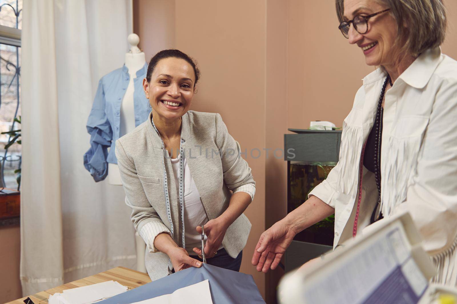Hispanic pretty woman, tailor cuts a fabric while sewing clothes in a fashion design workshop. Seamstress, sewer, tailoring, creation on new garment. Fashion designer business start-up concepT
