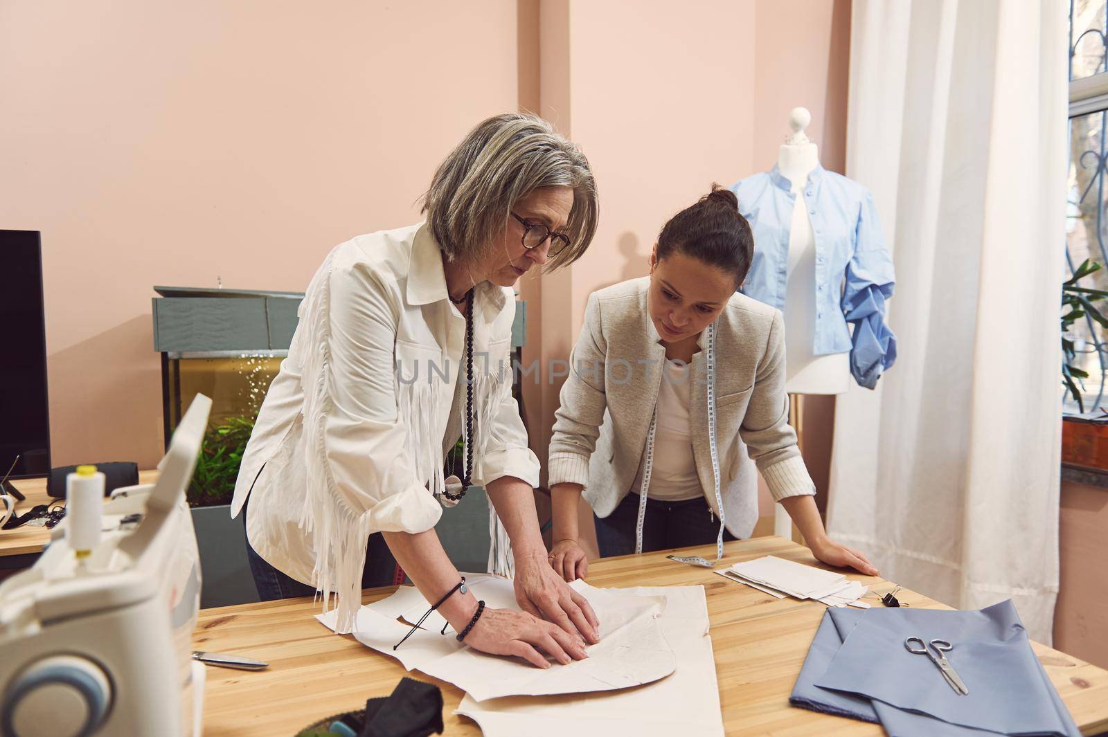 Skilled Fashion designers carefully create new fashionable styles, discuss patterns, take measurements during the development of new collection of handmade clothes in fashion design tailoring atelier