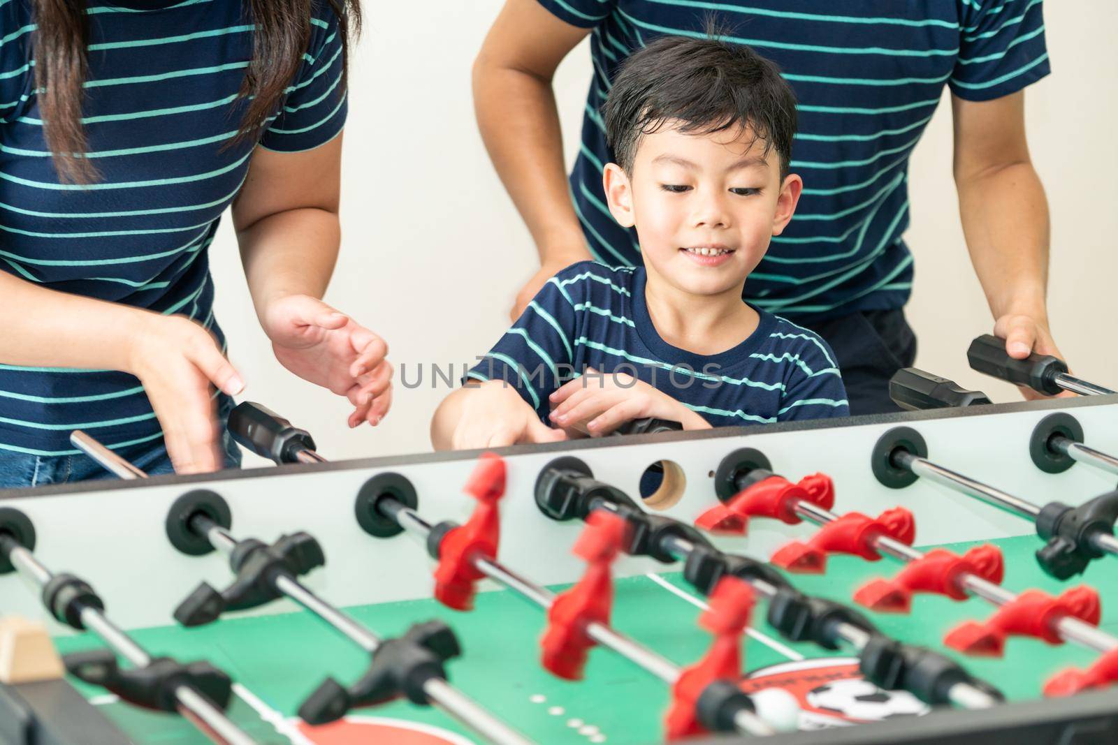Happy kid playing foosball table soccer with family, father and mother.