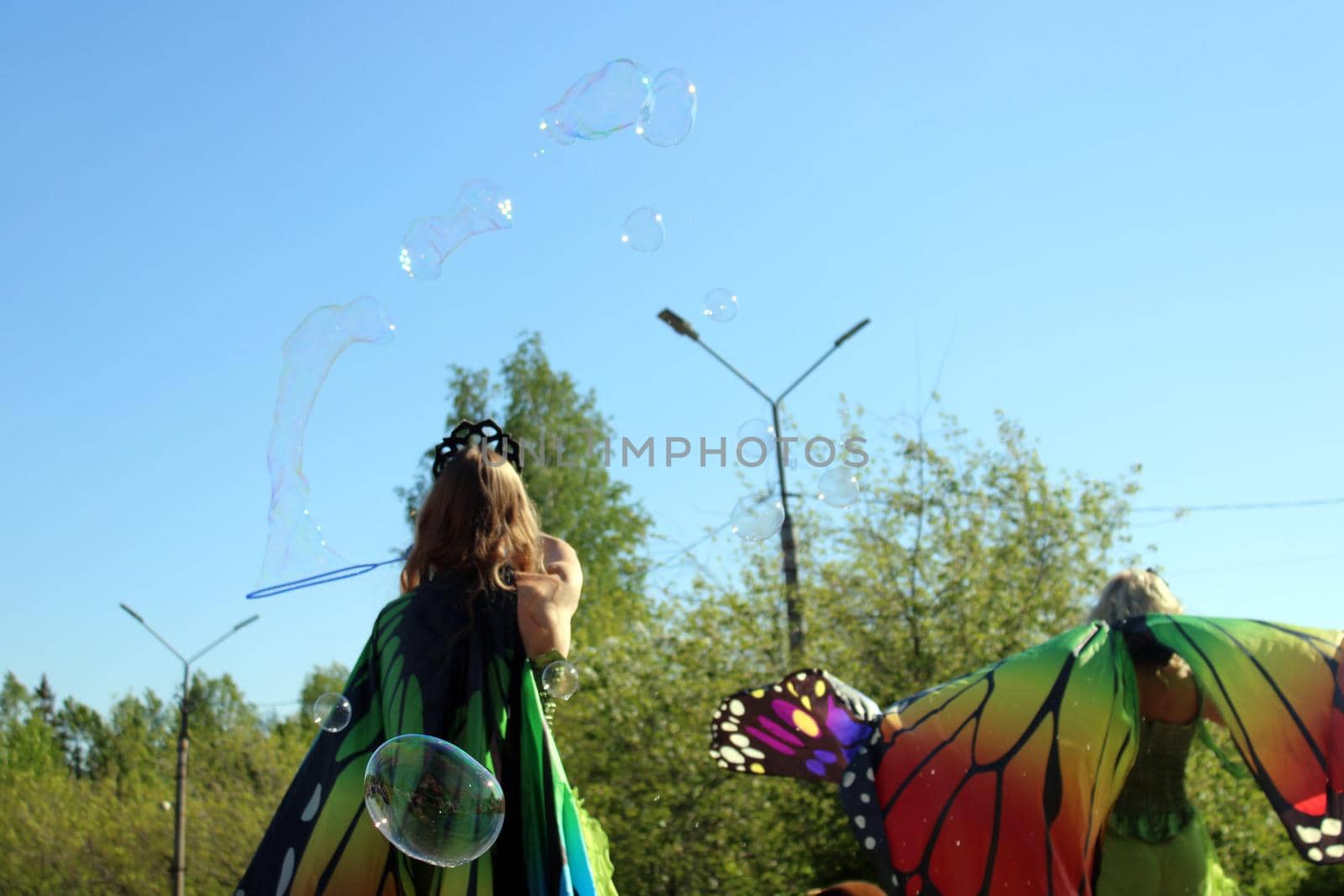 A girl in a colorful butterfly costume blows soap bubbles. Carnival..