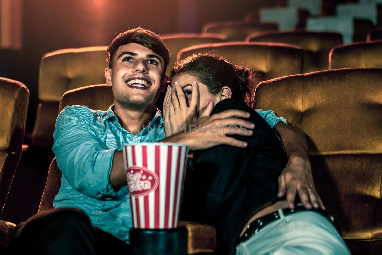 A couple of caucasian watch a thriller movie in the cinema, woman eyes closed and turning her face away from the screen