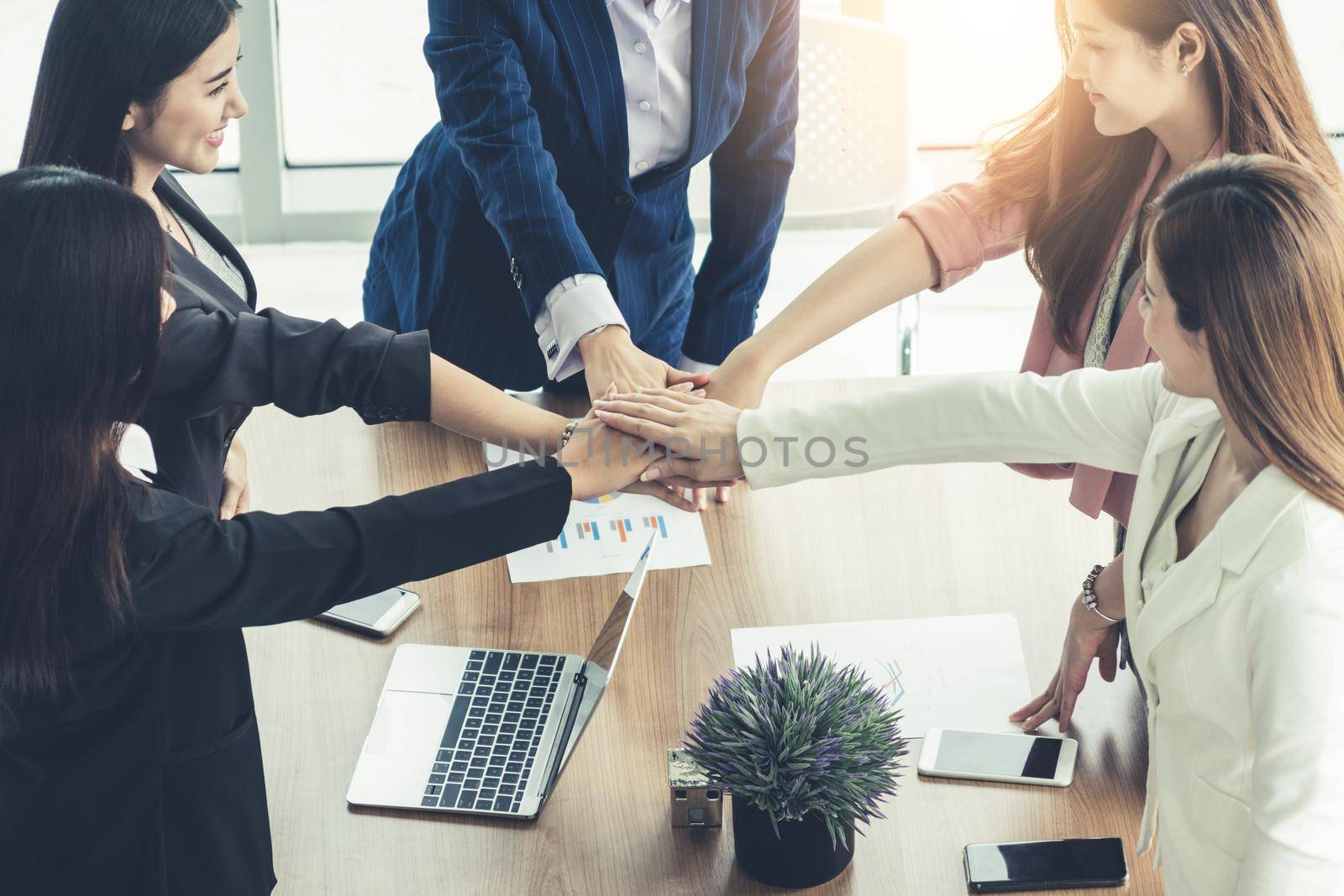 Businesswomen joining hands in group meeting at modern office room showing teamwork, support and unity in work and business. Female power and femininity concept.