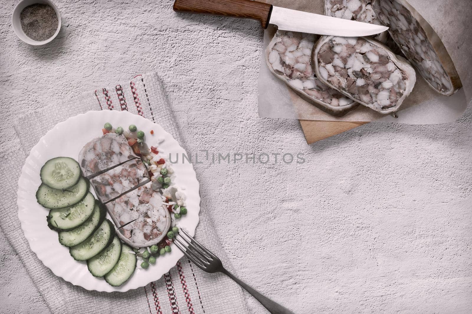 On the table on a plate of delicious meat appetizer: stuffed with meat and bacon pork stomach, sliced, next to vegetables and fresh cucumbers. Top view, copy space, flat lay