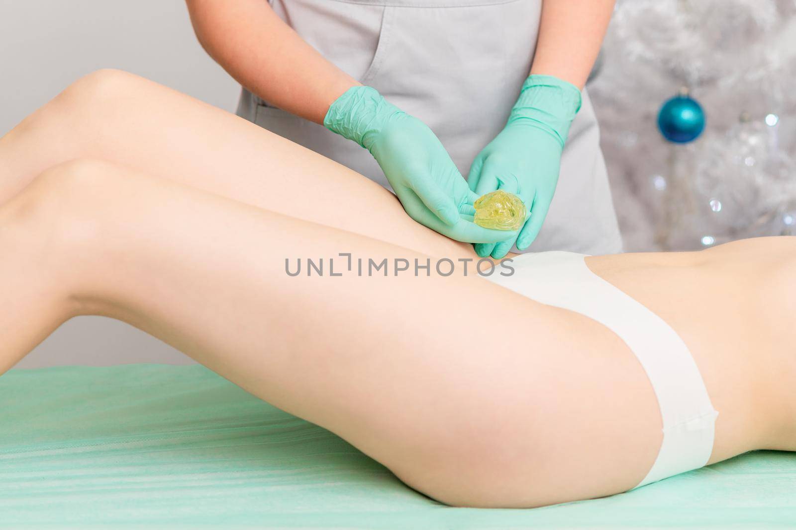 Beautician waxing female legs in spa center.