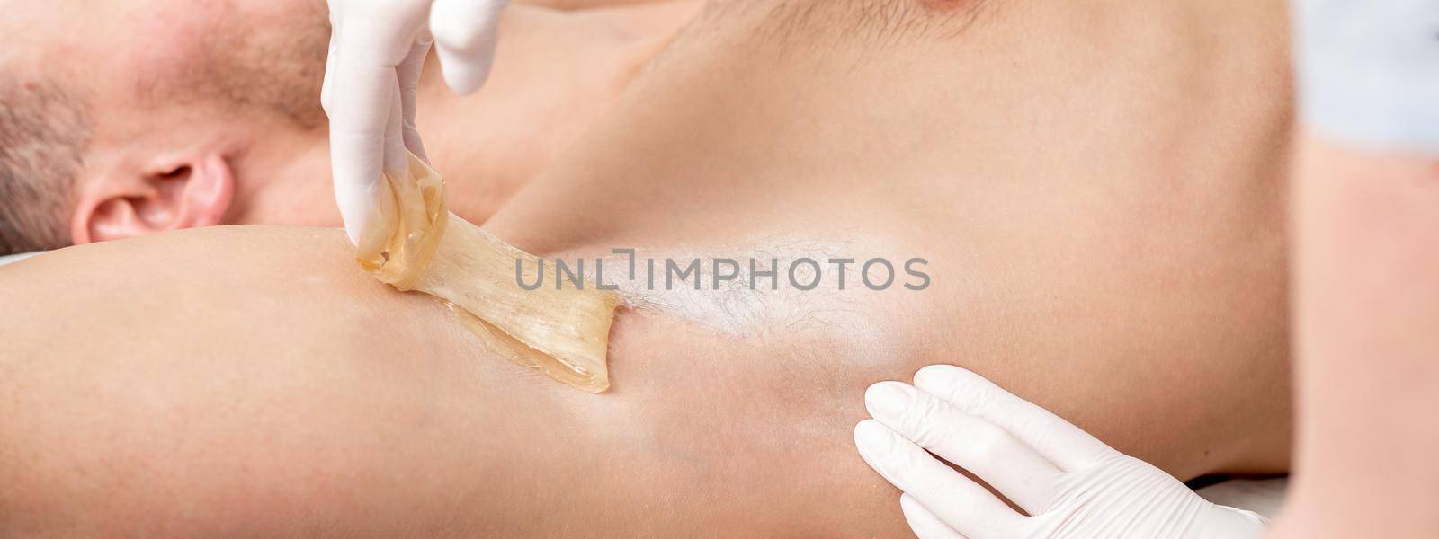 Depilation and epilation male armpit with liquid sugar paste. Hand of cosmetologist applying wax paste on armpit of man. Smooth underarm concept