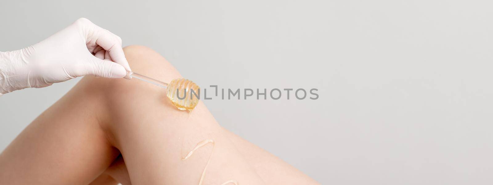 Wax on honey stick flowing down on female leg in human hand wearing protective glove on white background