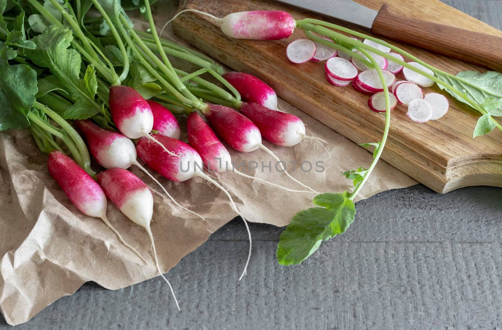 On the wooden surface of the table is a bunch of young radishes with green leaves.