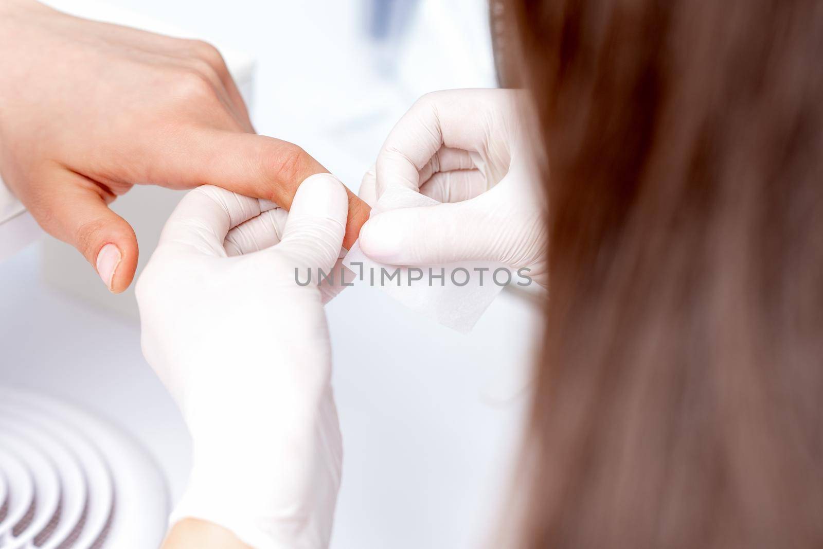 Manicure master removing nail polish with white cotton pad in beauty salon