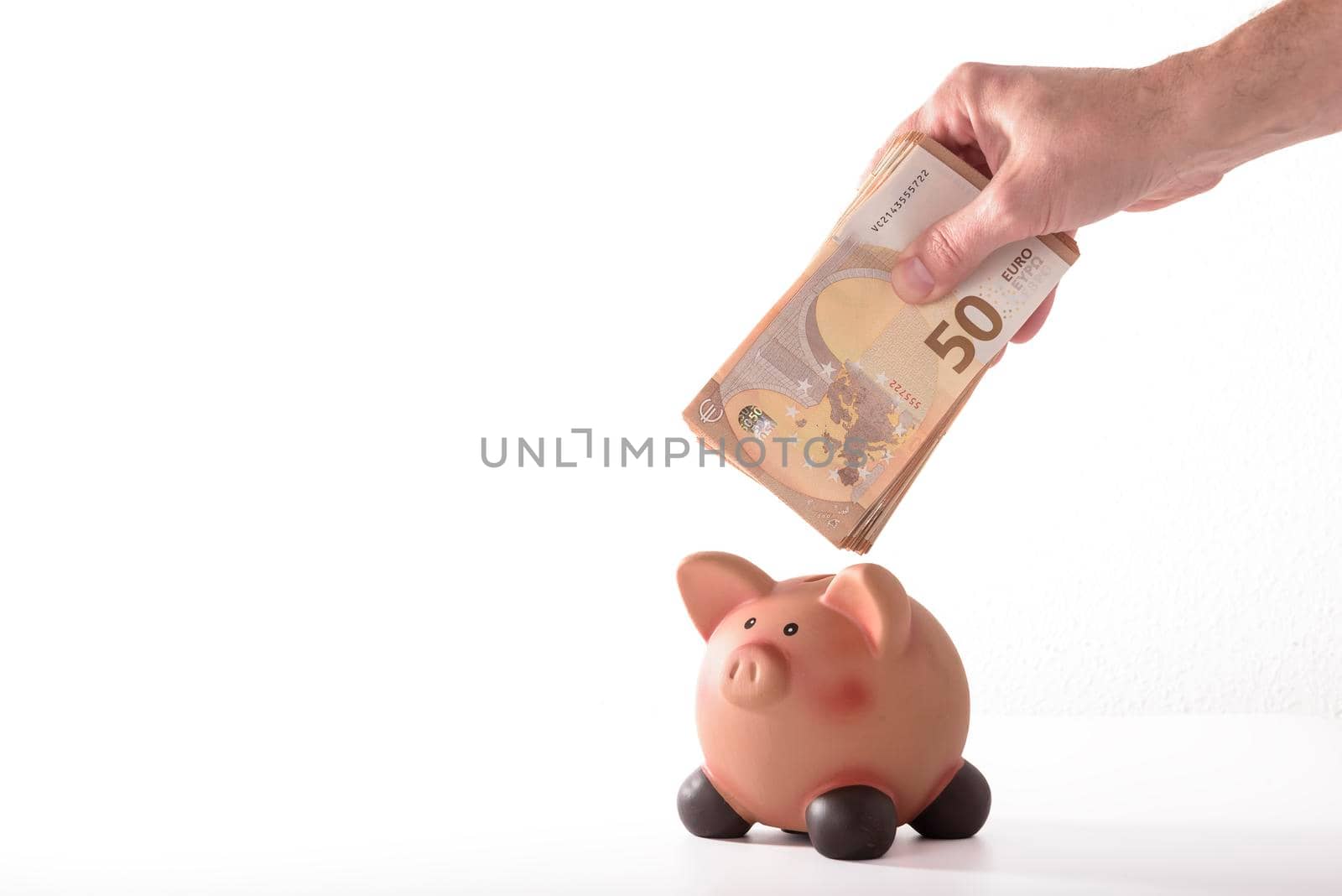 detail of a hand inserting a fifty euro banknote into a piggy bank, concept for business and save money on white background