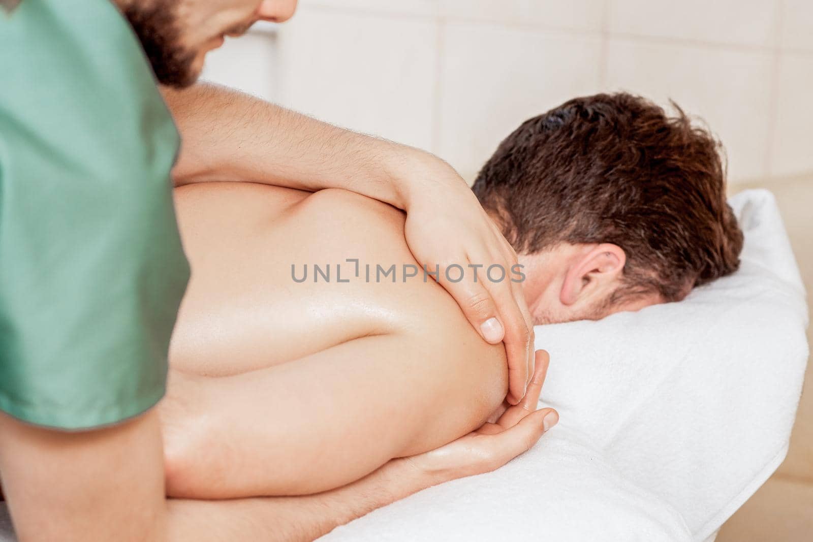 Young man receiving professional massage on shoulder by male massage therapist close up.