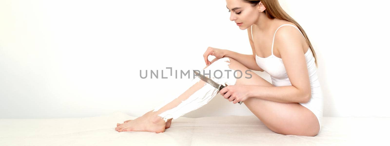 Beautiful young caucasian woman shaves her legs with a knife on a white background