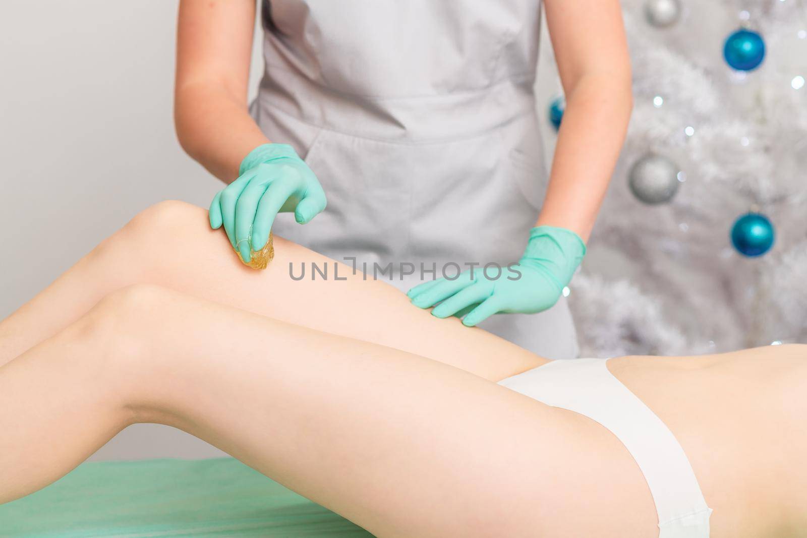 Beautician waxing female legs in spa center.