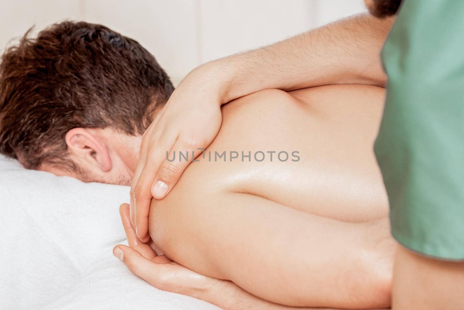 Close-up of massage therapist hands doing wellness massage on man shoulder in spa.