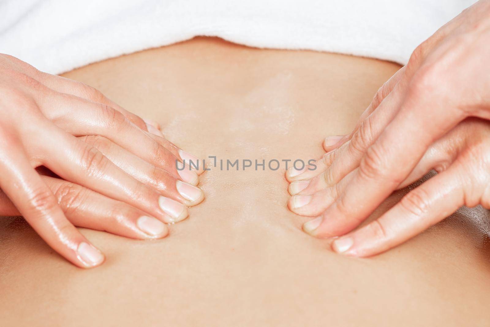 Man receiving back massage in four hands of two male therapists close up.