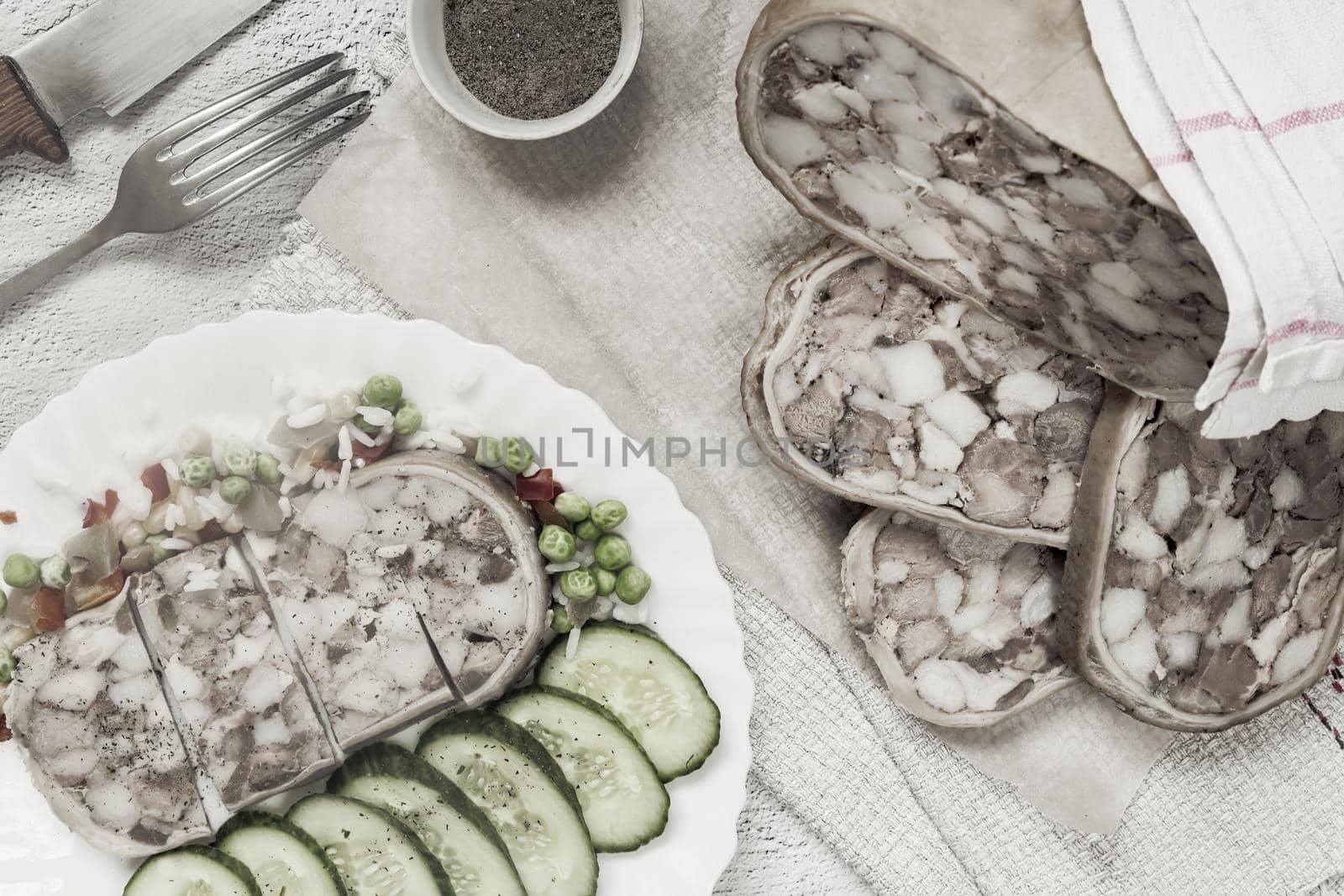 On the table on a plate of delicious meat appetizer: stuffed with meat and bacon pork stomach, sliced, next to vegetables and fresh cucumbers. Top view, flat lay