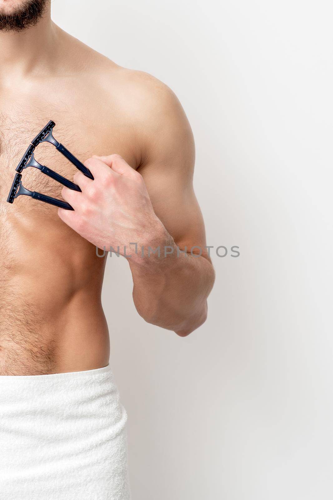 Young caucasian man with beard holds razor shaves his chest with white shaving foam on white background. Man shaving his torso