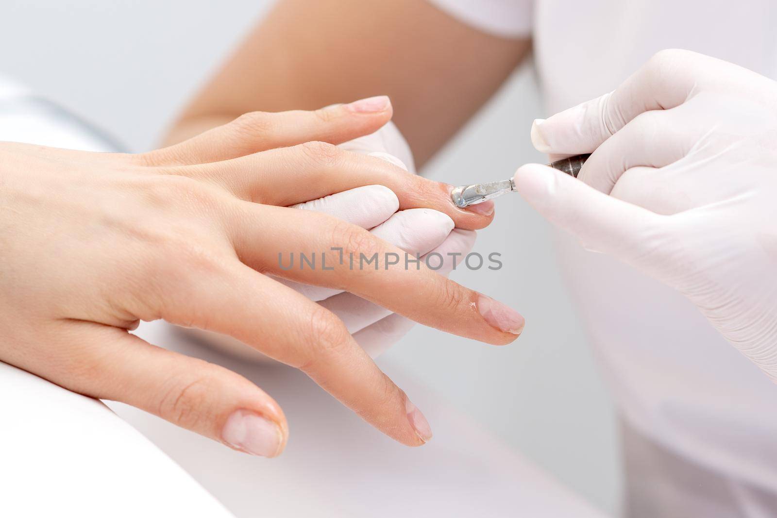 Hands of manicurist pushing cuticles on female's nails with manicure tool. Woman receiving manicure and nail care procedure