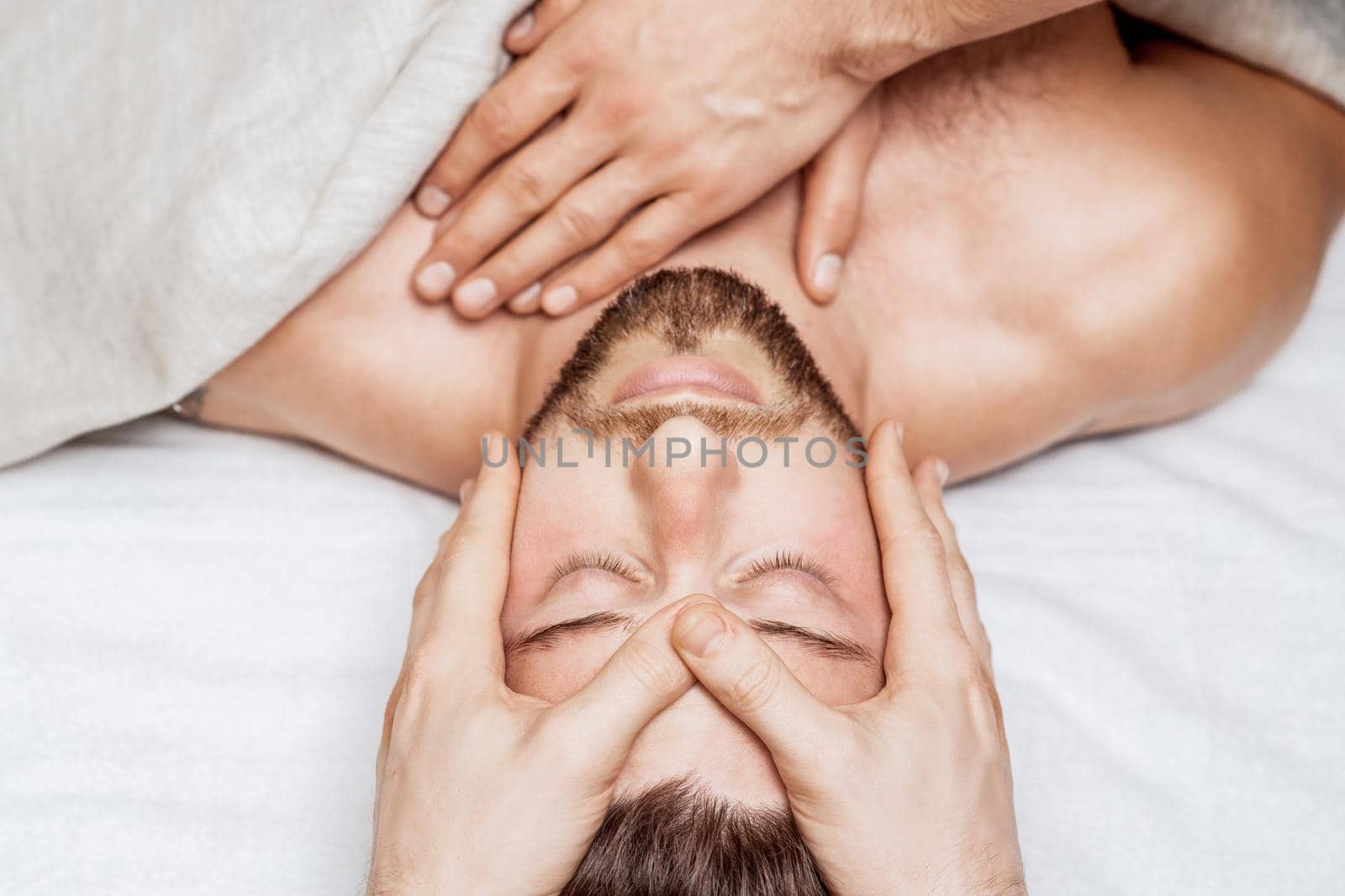 Top view of relaxing young caucasian man enjoying head massage by two masseurs
