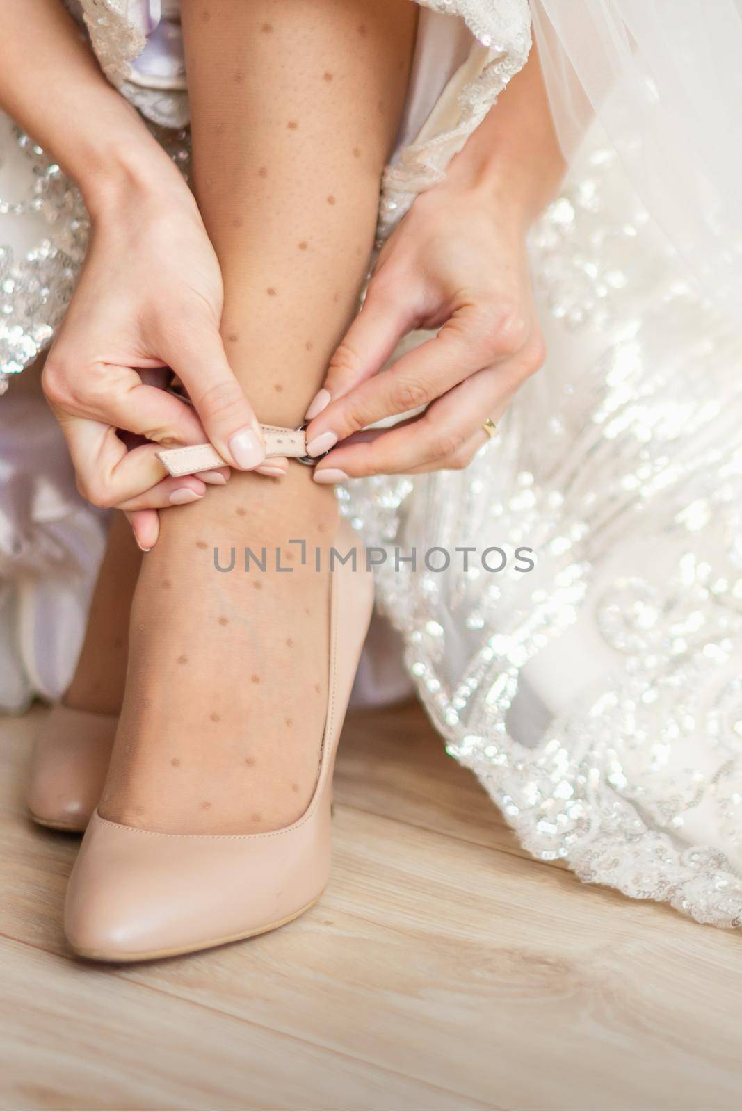 Bride puts on wedding shoes on her feet wearing beautiful wedding dress