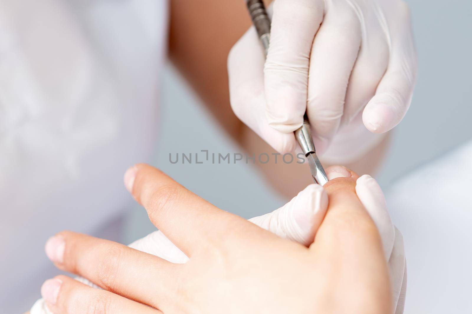 Hands of manicurist pushing cuticles on female's nails with manicure tool. Woman receiving manicure and nail care procedure