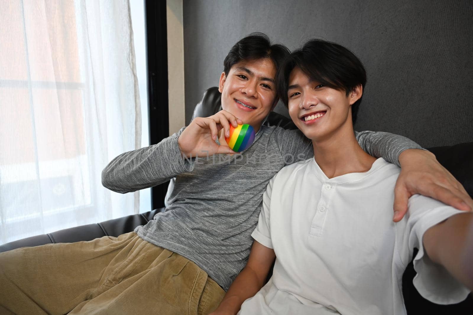 Young gay couple embracing and holding rainbow heart shape. LGBT, pride, relationships and equality concept.