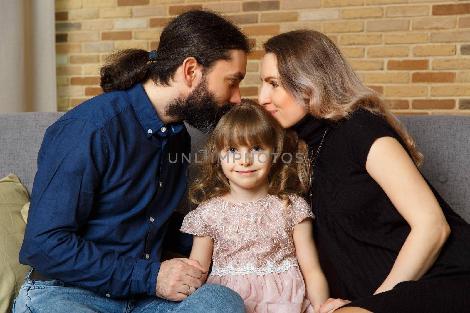 Happy young father, mother and daughter sit on wicker sofa at home. The image of a happy family expecting the second child, studio