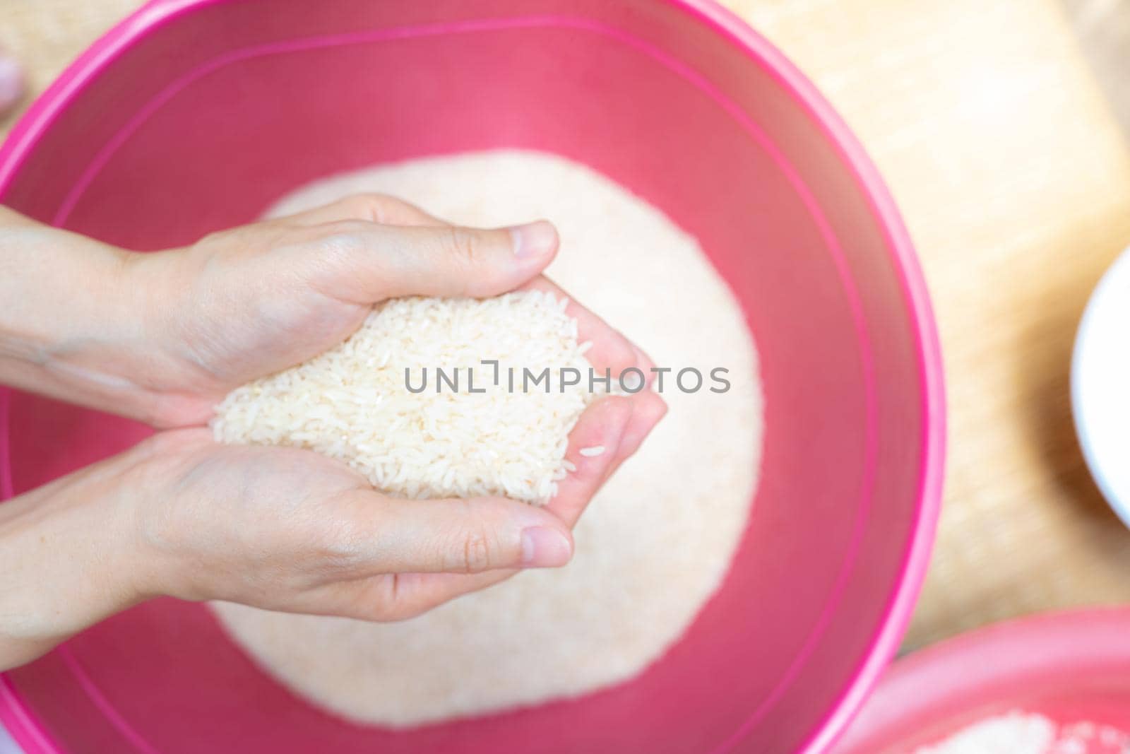 Top view woman hand holding rice above red plastic bowl. Global food crisis. Raw dry rice. Uncooked milled white rice. Zakat and charity concept. Organic cereal grain. Rice price in world market. 