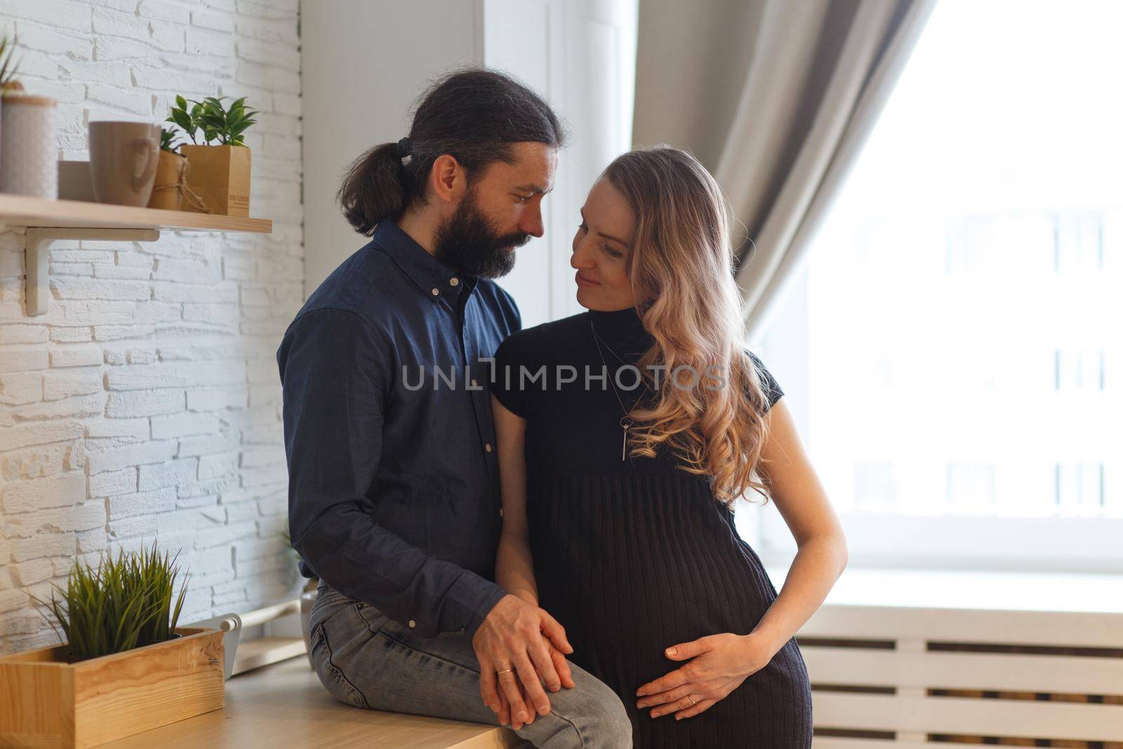 Man embracing pregnant partner in kitchen. by BY-_-BY