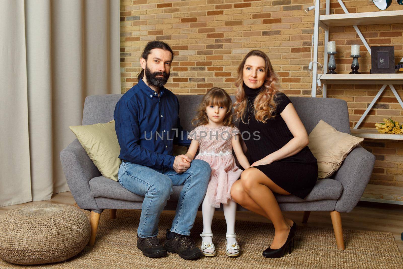 Happy young father, mother and daughter sit on wicker sofa at home. The image of a happy family expecting the second child, studio