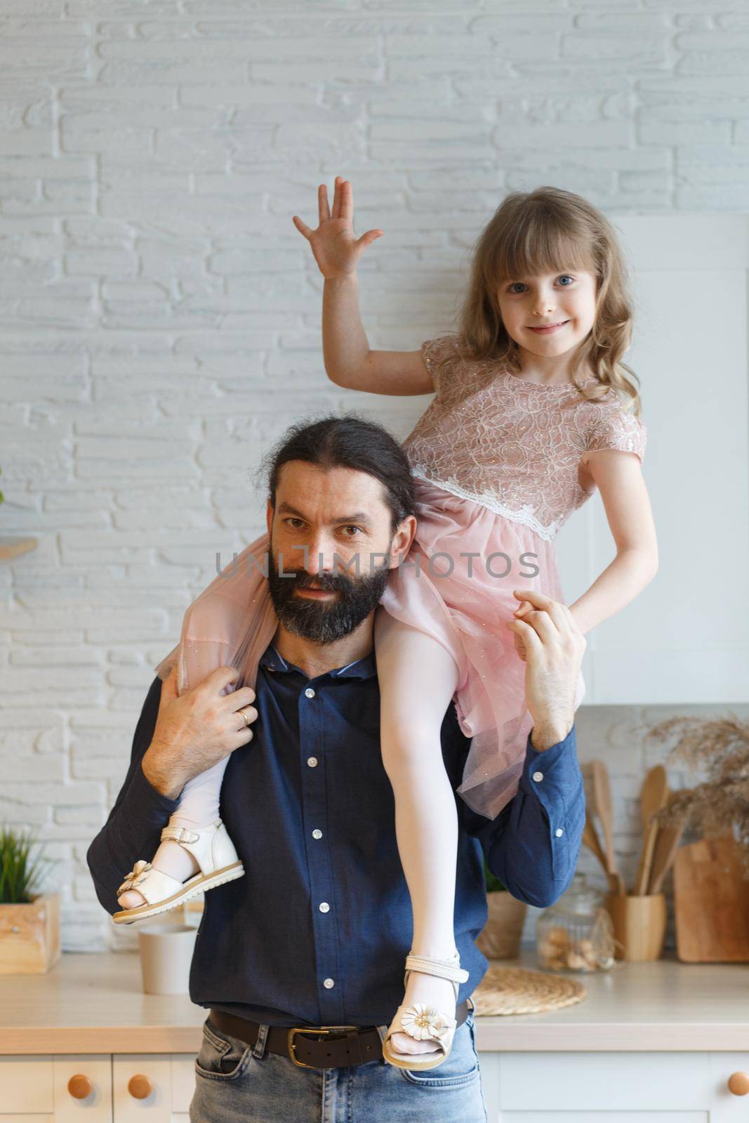 Happy little daughter sitting on father neck piggybacking playing active game at home. Smiling dad holding cute girl with arms outstretched carrying on back. Family spending weekend together.