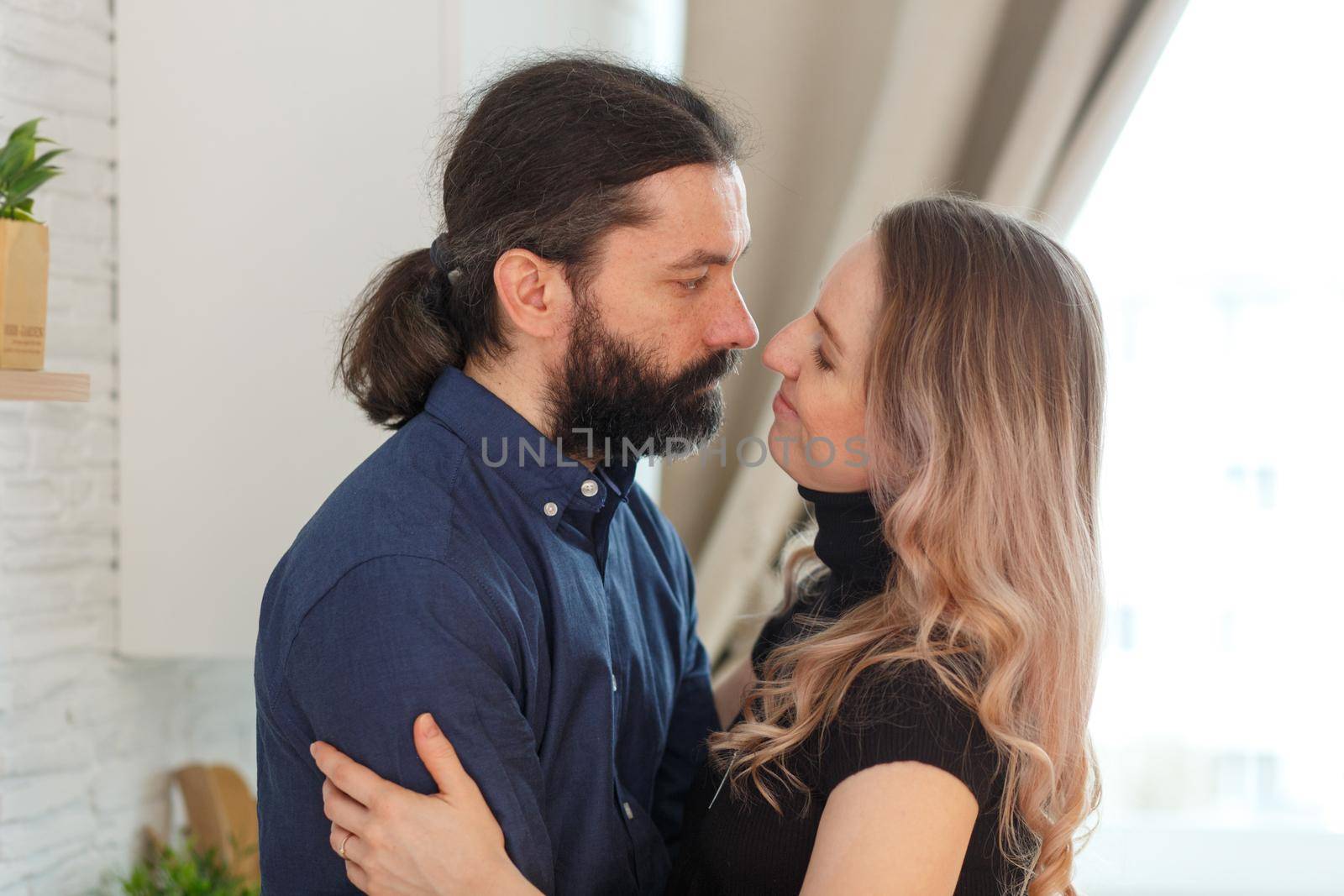 Man embracing pregnant partner in kitchen. Adult family pregnancy concept. Future parents in home outfit embrace standing in the kitchen, looking at each other, kissing. Healthy Lifestyle.