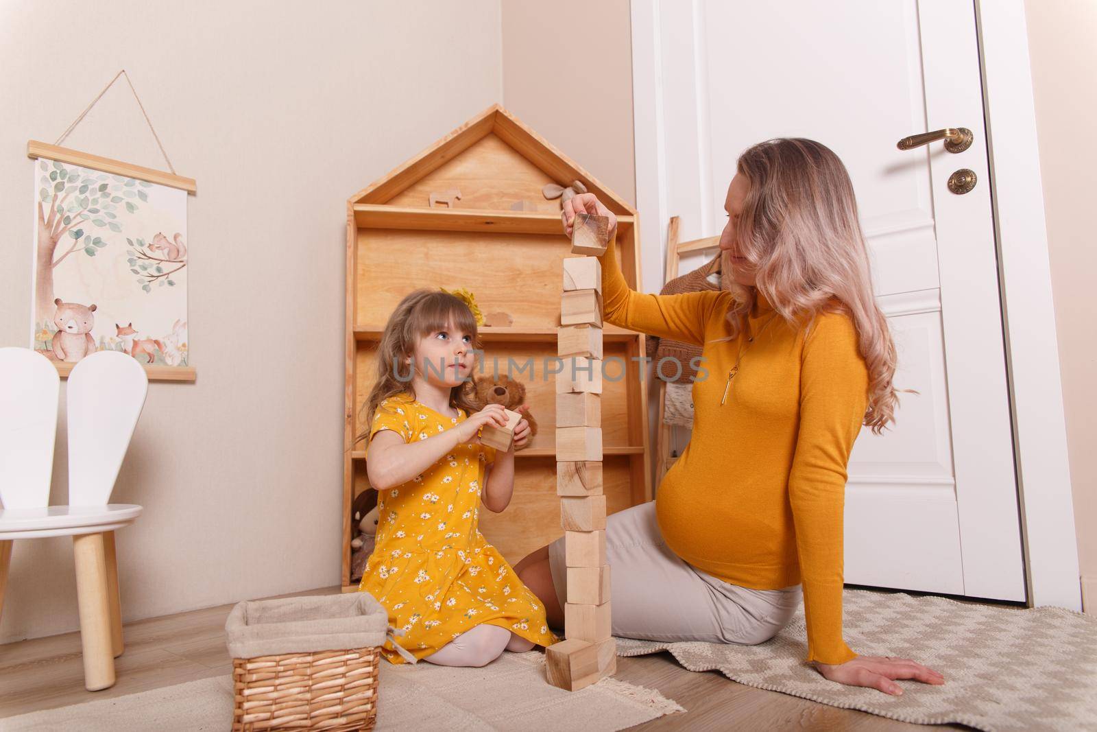 A pregnant woman plays in the nursery with her daughter. They build a tower out of wooden blocks.