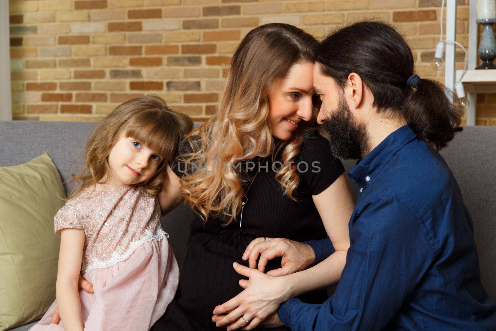 Happy young father, mother and daughter sit on wicker sofa at home. The image of a happy family expecting the second child, studio