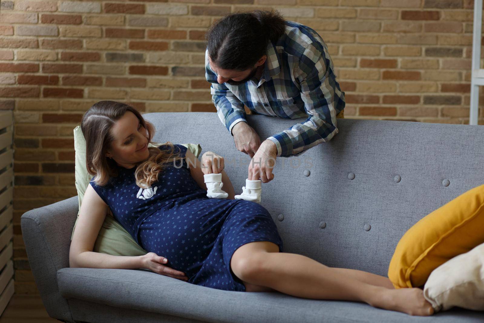 An adult couple in love waiting for a child. A man and his pregnant wife are playing on a sofa at home