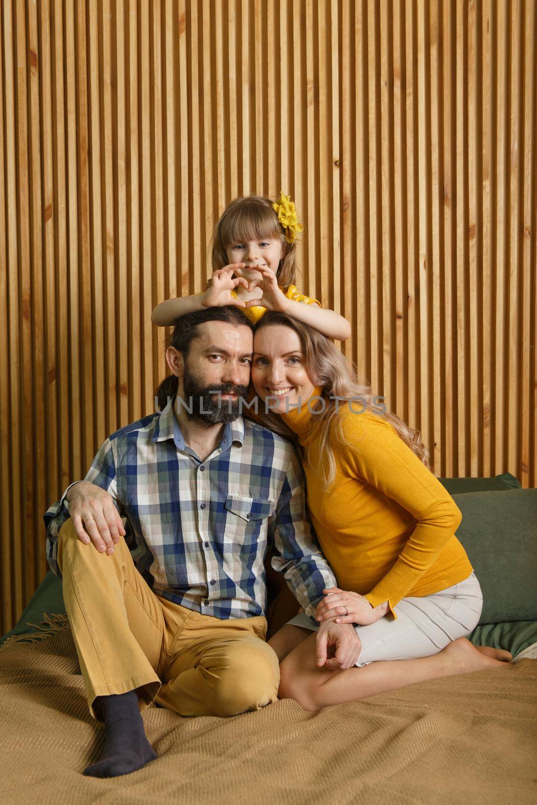 Happy family is having fun in bedroom. Enjoying being together. Parents are tickling their little daughter while lying in bed. Father, daughter and pregnant mother.