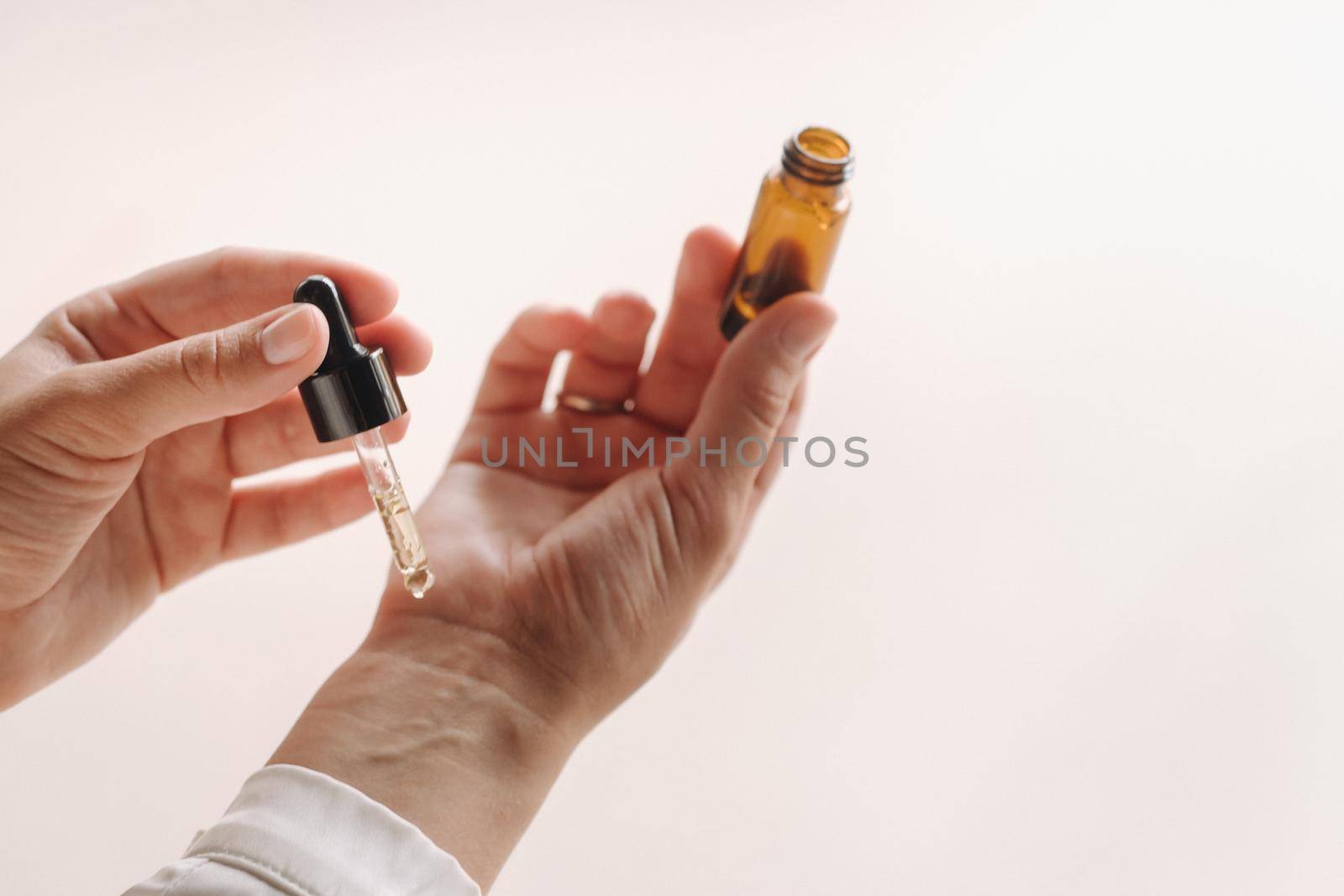 Close-up of a Woman's hands applying essential oil on her wrist indoors by Lobachad