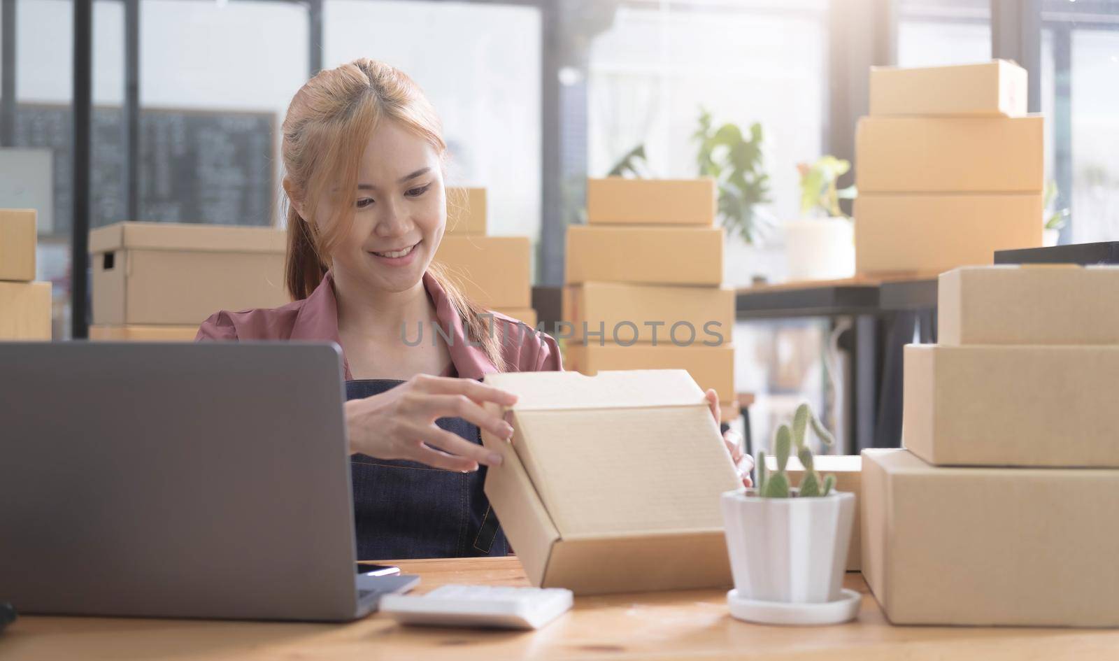 Happy young asian woman startup small business freelance holding parcel box and computer laptop and sitting on chair, Online marketing packing box delivery concept by wichayada