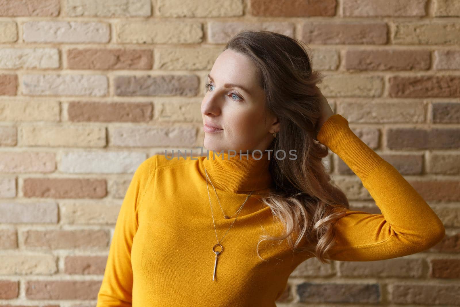 Thoughtful pregnant woman in yellow cardigan caressing her belly and posing near by brick wall
